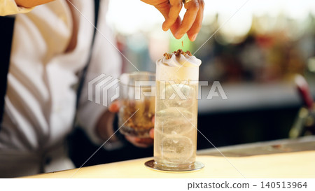 Bartender garnishing cocktail with whipped cream and nuts Bartender garnishing cocktail with whipped cream and nuts 140513964