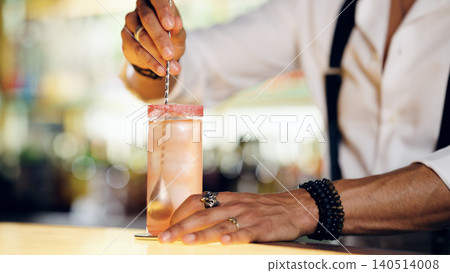 Bartender stirring a pink cocktail with a bar spoon Bartender stirring a pink cocktail with a bar spoon 140514008