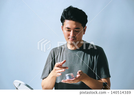 A Japanese male office worker in his 30s picks up a skincare product and tries to apply it to his face. A Japanese male office worker in his 30s picks up a skincare product and tries to apply it to his face. 140514389