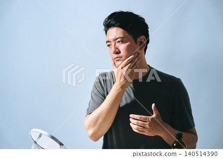 一位三十多歲的日本男子,公司職員,在進行護膚程序時,用手撫摸著臉,看著鏡子。 一位三十多歲的日本男子,公司職員,在進行護膚程序時,用手撫摸著臉,看著鏡子。 140514390