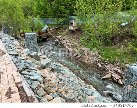 Rocky riverbank with rubble and construction debris along narrow stream channel in urban area 140514702