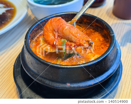 Sundubu, a Korean dish served in an earthenware pot. A piping hot, spicy soup with vegetables and tofu. A close-up of a shrimp. Sundubu, a Korean dish served in an earthenware pot. A piping hot, spicy soup with vegetables and tofu. A close-up of a shrimp. 140514900