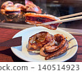烤魷魚，一道盛放在熱鐵板上的料理。圖片中有人正用筷子夾起美味的烤魷魚。 140514923