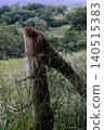 Old wooden fence post with barbed wire line separating long grass field 140515383