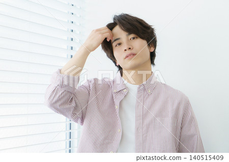 A portrait of a young Japanese man wearing a pinstripe shirt standing by a window. A portrait of a young Japanese man wearing a pinstripe shirt standing by a window. 140515409