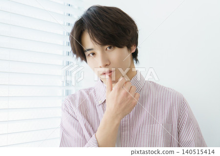 A portrait of a young Japanese man wearing a pinstripe shirt standing by a window. A portrait of a young Japanese man wearing a pinstripe shirt standing by a window. 140515414
