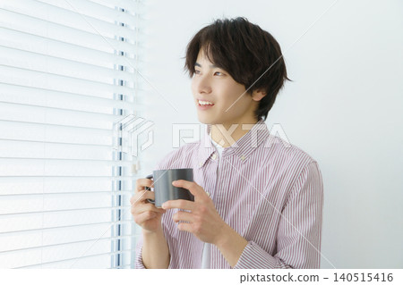 A portrait of a young Japanese man standing by a window, wearing a pinstripe shirt and holding a mug. A portrait of a young Japanese man standing by a window, wearing a pinstripe shirt and holding a mug. 140515416