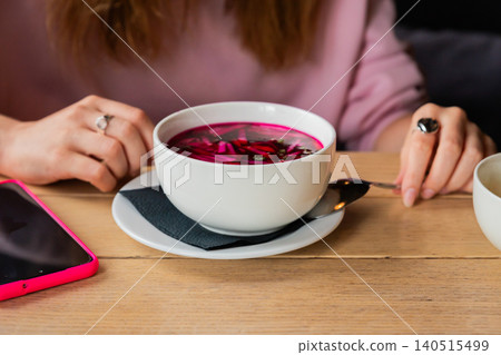 Woman eating cold beet soup in restaurant. Traditional summer vegetable borscht or svehkolnik in white bowl. Healthy lunch meal, culinary concept of Eastern European kitchen culture. Woman eating cold beet soup in restaurant. Traditional summer vegetable borscht or svehkolnik in white bowl. Healthy lunch meal, culinary concept of Eastern European kitchen culture. 140515499