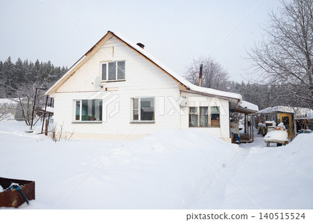 White country house with snow covered yard on a cold Winter day. Rural home with snowdrifts outside. Concept of a winter season. White country house with snow covered yard on a cold Winter day. Rural home with snowdrifts outside. Concept of a winter season. 140515524