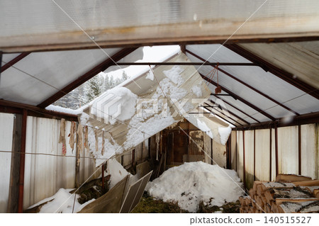 Damaged greenhouse roof collapsed under heavy snow load. Winter impact on agriculture building. Scene of natural disaster. Damaged greenhouse roof collapsed under heavy snow load. Winter impact on agriculture building. Scene of natural disaster. 140515527