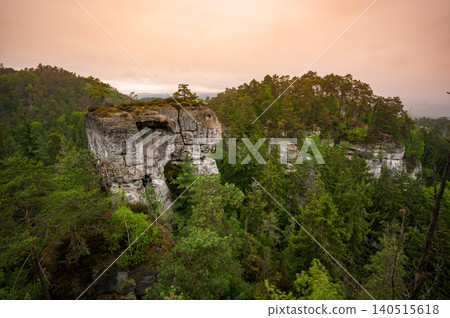 Rock city formations in Hruba Skala, Bohemian Paradise (Cesky raj), rising from forest seen from above. Orange sunrise sky lights sandstone towers and valleys panoramic view sky . Rock city formations in Hruba Skala, Bohemian Paradise (Cesky raj), rising from forest seen from above. Orange sunrise sky lights sandstone towers and valleys panoramic view sky . 140515618