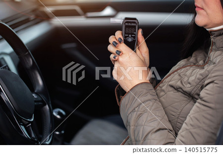 Female Driver Sits Inside Car Checking Breathalyzer Results. Woman Looking At Alcohol Test Device. Female Driver Sits Inside Car Checking Breathalyzer Results. Woman Looking At Alcohol Test Device. 140515775