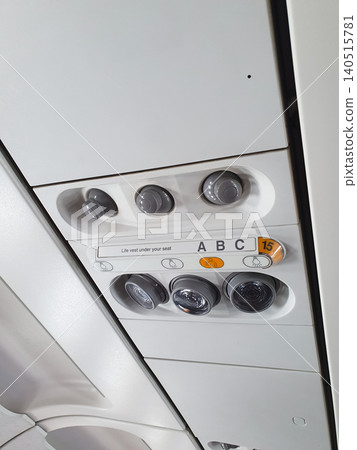 Airplane ceiling panel with air conditioning vents and reading lights above seat row. Aviation interior equipment for passenger comfort and cabin safety control in commercial aircraft. Airplane ceiling panel with air conditioning vents and reading lights above seat row. Aviation interior equipment for passenger comfort and cabin safety control in commercial aircraft. 140515781