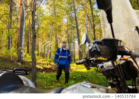 Berry picker with basket exploring forest and quadbike or ATV parked nearby Berry picker with basket exploring forest and quadbike or ATV parked nearby 140515784