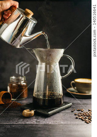 Pour hot water over coffee brewing with dripper and kettle, specialty coffee preparation, dark background, still life Pour hot water over coffee brewing with dripper and kettle, specialty coffee preparation, dark background, still life 140516641