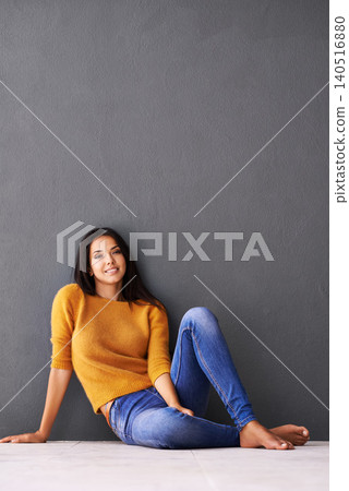 Portrait, girl and relax or chill on floor with casual outfit for fashion or comfort, leisure and wellness with smile. Female person, isolated with grey background or wall for clothing with mockup. 140516880