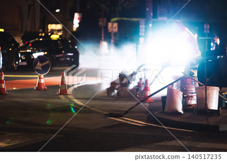 Night road works - worker repainting lane markings with machine and traffic cones in city street Night road works - worker repainting lane markings with machine and traffic cones in city street 140517235