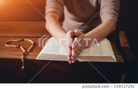 Christian woman praying in church. Hands crossed and Holy Bible on wooden desk. Christian woman praying in church. Hands crossed and Holy Bible on wooden desk. 140517292
