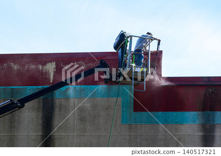 Worker pressure washing commercial building facade from aerial lift during exterior cleaning work Worker pressure washing commercial building facade from aerial lift during exterior cleaning work 140517321