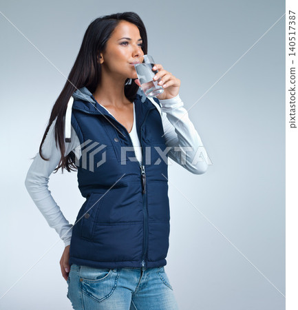 Woman, drink water for health and hydration in studio, nutrition and wellness with thirst on grey background. Liquid, aqua and mineral with h2o in glass, fresh and clean for refreshment and detox 140517387