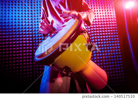 Young man playing on djembe in sound recording studio. Young man playing on djembe in sound recording studio. 140517510