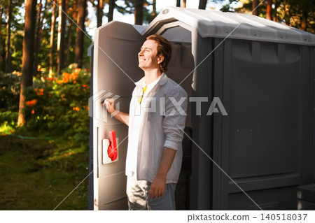 a man finds relief from an upset stomach and diarrhea, smiling as he exits a portable outdoor toilet after a gastrointestinal emergency. 140518037