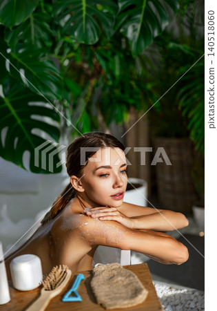 Caucasian young woman applying body scrub in bright modern home bathroom spa Caucasian young woman applying body scrub in bright modern home bathroom spa 140518060