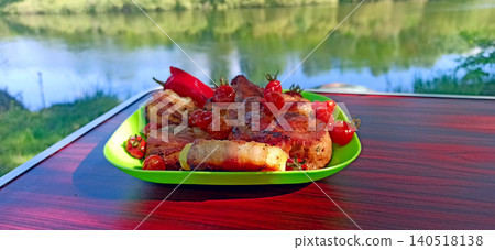 Grilled meat and bacon wrapped potatoes served with cherry tomatoes near a river Grilled meat and bacon wrapped potatoes served with cherry tomatoes near a river 140518138