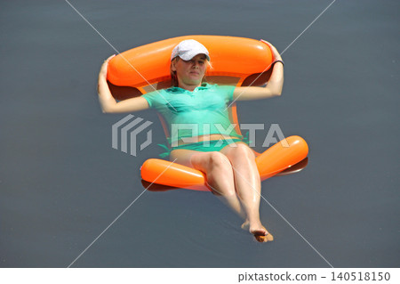 Young woman relaxing on orange inflatable floating chair in calm dark water Young woman relaxing on orange inflatable floating chair in calm dark water 140518150