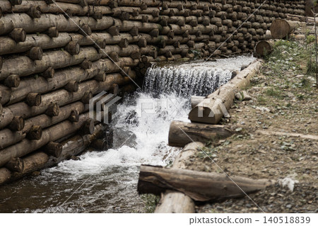 Mountain stream flowing past rustic log retaining wall structure in forest Mountain stream flowing past rustic log retaining wall structure in forest 140518839