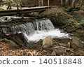 Small waterfall flowing under wooden footbridge in forest 140518848