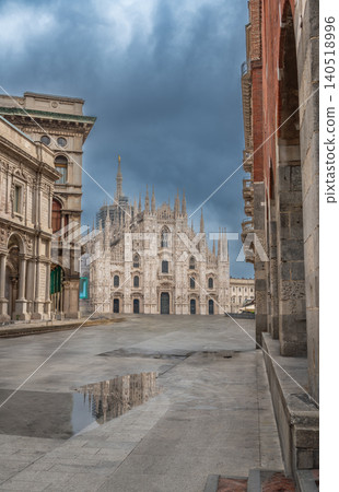 Milan, italy, october 2, 2024. Milan duomo cathedral dominating an empty piazza del duomo with a cloudy sky and reflection in a puddle, autumn in italy Milan, italy, october 2, 2024. Milan duomo cathedral dominating an empty piazza del duomo with a cloudy sky and reflection in a puddle, autumn in italy 140518996