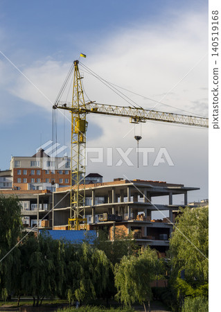 Large yellow crane next to a modern high-rise building under construction against a blue sky Large yellow crane next to a modern high-rise building under construction against a blue sky 140519168