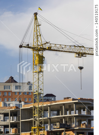 Yellow tower crane machinery operating over an unfinished concrete building frame Yellow tower crane machinery operating over an unfinished concrete building frame 140519175