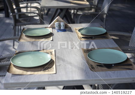 Served restaurant wooden table with light green plates and wicker chairs Served restaurant wooden table with light green plates and wicker chairs 140519227