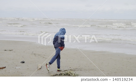 Beach Walk Serenity. Lone Person In Hoodie Advances Across Wet Beach With Scattered Timber And Foamy Waves . Creative Beach Walk Serenity. Lone Person In Hoodie Advances Across Wet Beach With Scattered Timber And Foamy Waves . Creative 140519234
