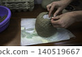 Mud Dome Crafting. Worker Carefully Sculpting Textured Clay Around Candle On Towelcovered Table. Media 140519667
