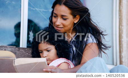 Latina mother daughter reading book together Latina mother daughter reading book together 140520536
