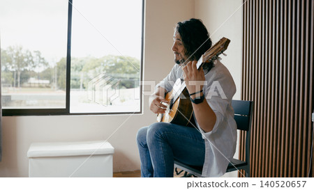 Man playing acoustic guitar near window at home Man playing acoustic guitar near window at home 140520657