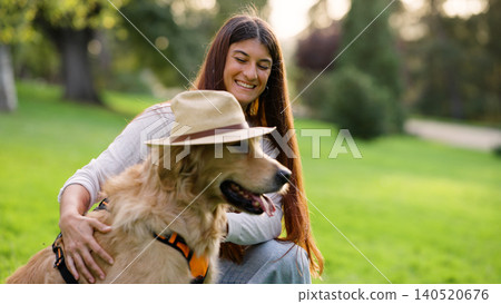 Woman smiling with golden retriever wearing hat in park Woman smiling with golden retriever wearing hat in park 140520676