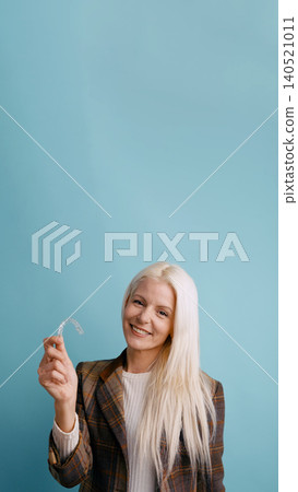 Woman smiling, holding clear plastic dental aligner 140521011