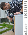 Man secures drawer side with cordless drill while holding the panel steady outdoors 140521371
