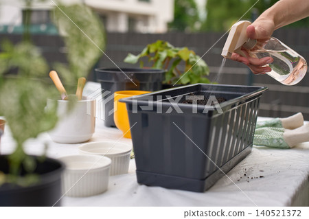 Woman sprays water on soil in planter box at outdoor gardening table 140521372