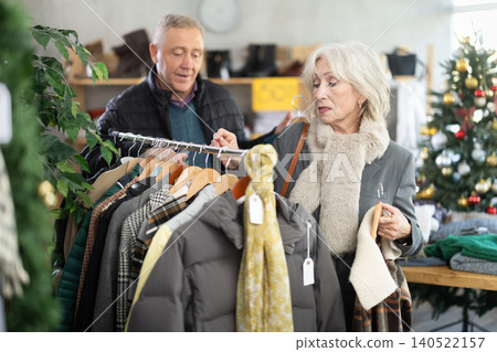 Elderly couple standing in Christmas shop and choosing jackets Elderly couple standing in Christmas shop and choosing jackets 140522157