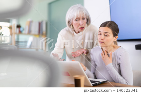 Elderly woman scolding adult female colleague working on laptop Elderly woman scolding adult female colleague working on laptop 140522341