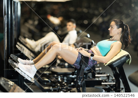 In gym, woman uses gym apparatus to pump up press. In gym, woman uses gym apparatus to pump up press. 140522546
