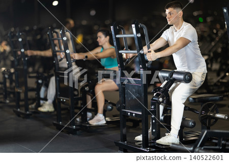 Guy performing sit-to-stand resistance exercise on machine at gym Guy performing sit-to-stand resistance exercise on machine at gym 140522601