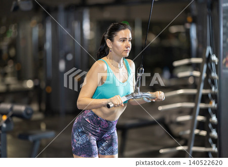 In gym, woman uses cable row machine to strengthen muscles. 140522620