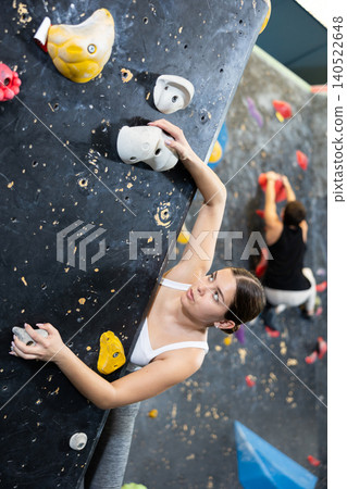 Female fitness climber training at bouldering gym. Young woman rise up on artificial climbing wall Female fitness climber training at bouldering gym. Young woman rise up on artificial climbing wall 140522648