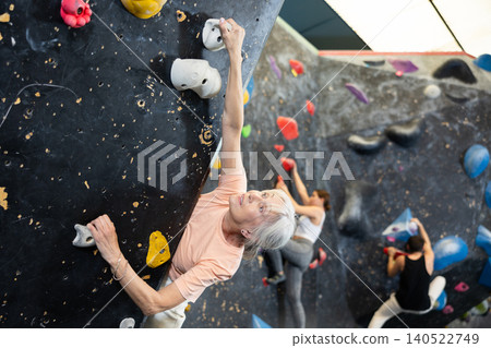 Determined senior woman doing her best at climbing artificial wall 140522749